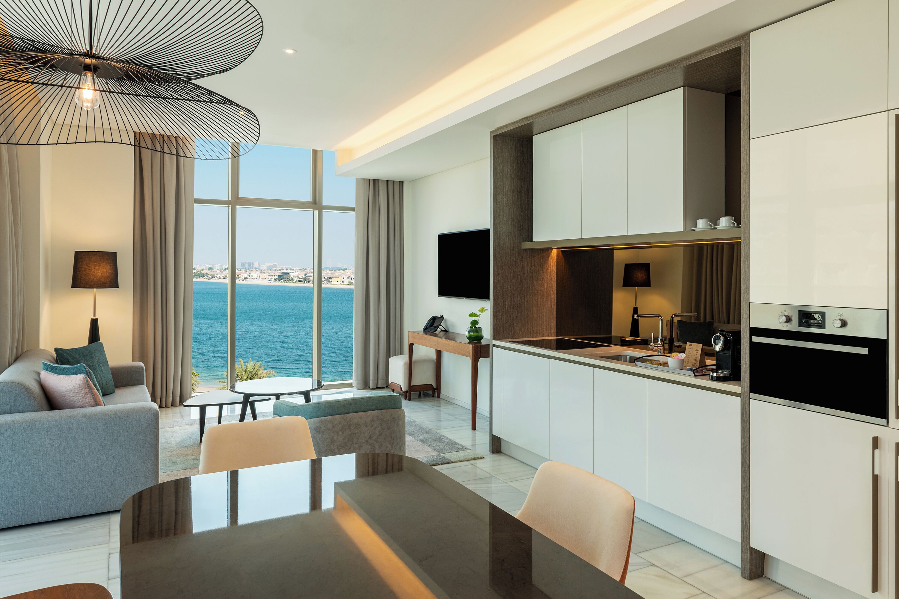 A modern living room with a large window overlooking the sea, a dining area, and a kitchen with built-in appliances.