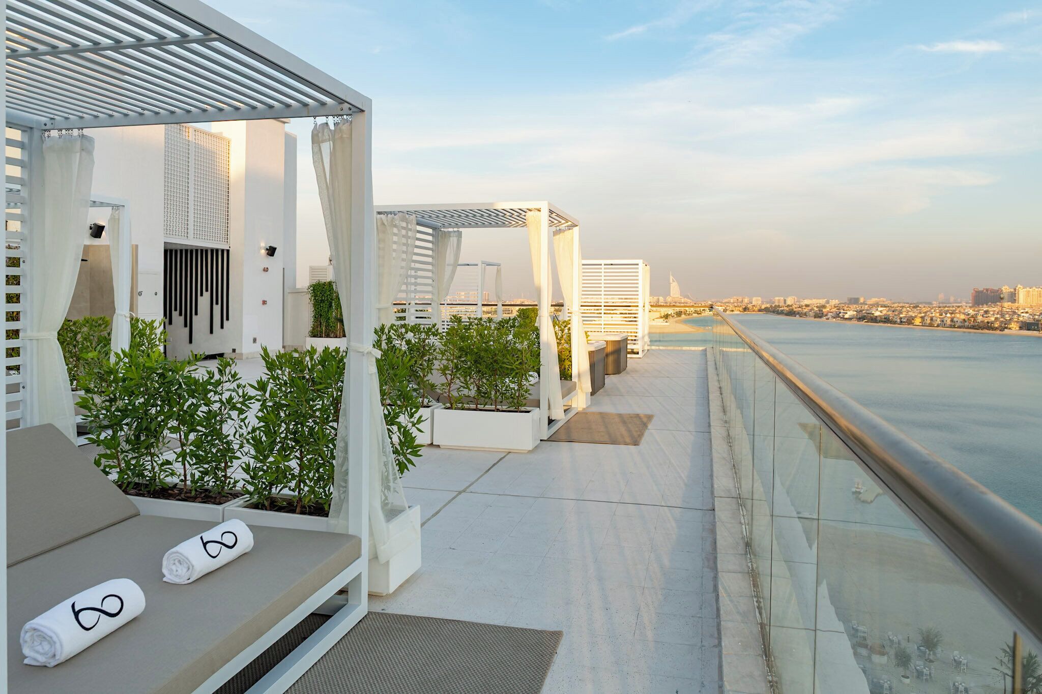 Een terras op het dak met witte lounge stoelen, een pergola en plantenbakken.