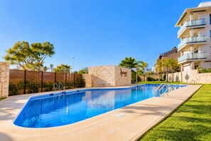 A swimming pool with a stone wall, a grassy area, and a multi-story building in the background. - Arenal Dream Penthouse I Javea Arenal  Luxury with Roof Terrace & only 150m from the Beach (Javea / Xàbia)