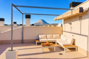A rooftop terrace with a sofa, a table with fruit, and a mountain view. - Arenal Dream Penthouse I Javea Arenal  Luxury with Roof Terrace & only 150m from the Beach (Javea / Xàbia)