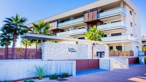 Een modern meerhoogbouw hotel met een stenen gevel, balkons en palmbomen.