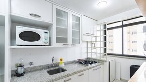 A compact kitchen with white cabinets, a microwave, a sink, and a stove. - Cool Duplex Studio Comfort & Great Location (São Paulo)