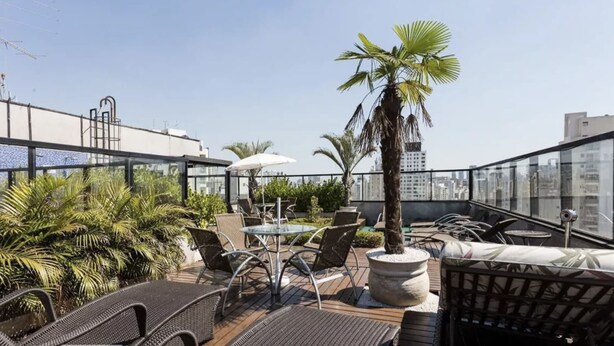 A rooftop terrace with outdoor seating, palm trees, and a city view. - Cool Duplex Studio Comfort & Great Location (São Paulo)