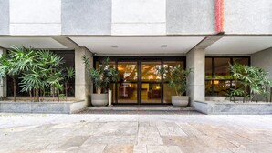 A building entrance with a stone-paved courtyard, large potted plants, and a glass door. - Cool Duplex Studio Comfort & Great Location (São Paulo)