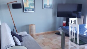 Un salon moderne avec un canapé, une table à manger et des chaises. Deux tableaux encadrés ornent le mur, ainsi qu’une lampe et un téléviseur.