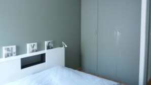 Une chambre à coucher avec un lit, une armoire et une étagère où sont exposés des tableaux encadrés.