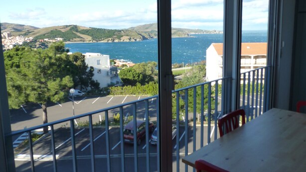 Un balcon avec vue sur une ville côtière, un espace de stationnement et une table avec des chaises.