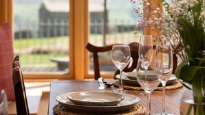 A dining table set with plates, glasses, and a vase of flowers, with a view of a building and greenery outside. - HEATHERDENE - Cottage set in the midst of the Yorkshire Dales with amazing views (Richmond)
