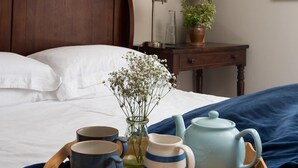 A neatly made bed with white linens, a wooden headboard, a bedside table with a lamp, a tray with mugs and a teapot, and a vase with flowers. - HEATHERDENE - Cottage set in the midst of the Yorkshire Dales with amazing views (Richmond)
