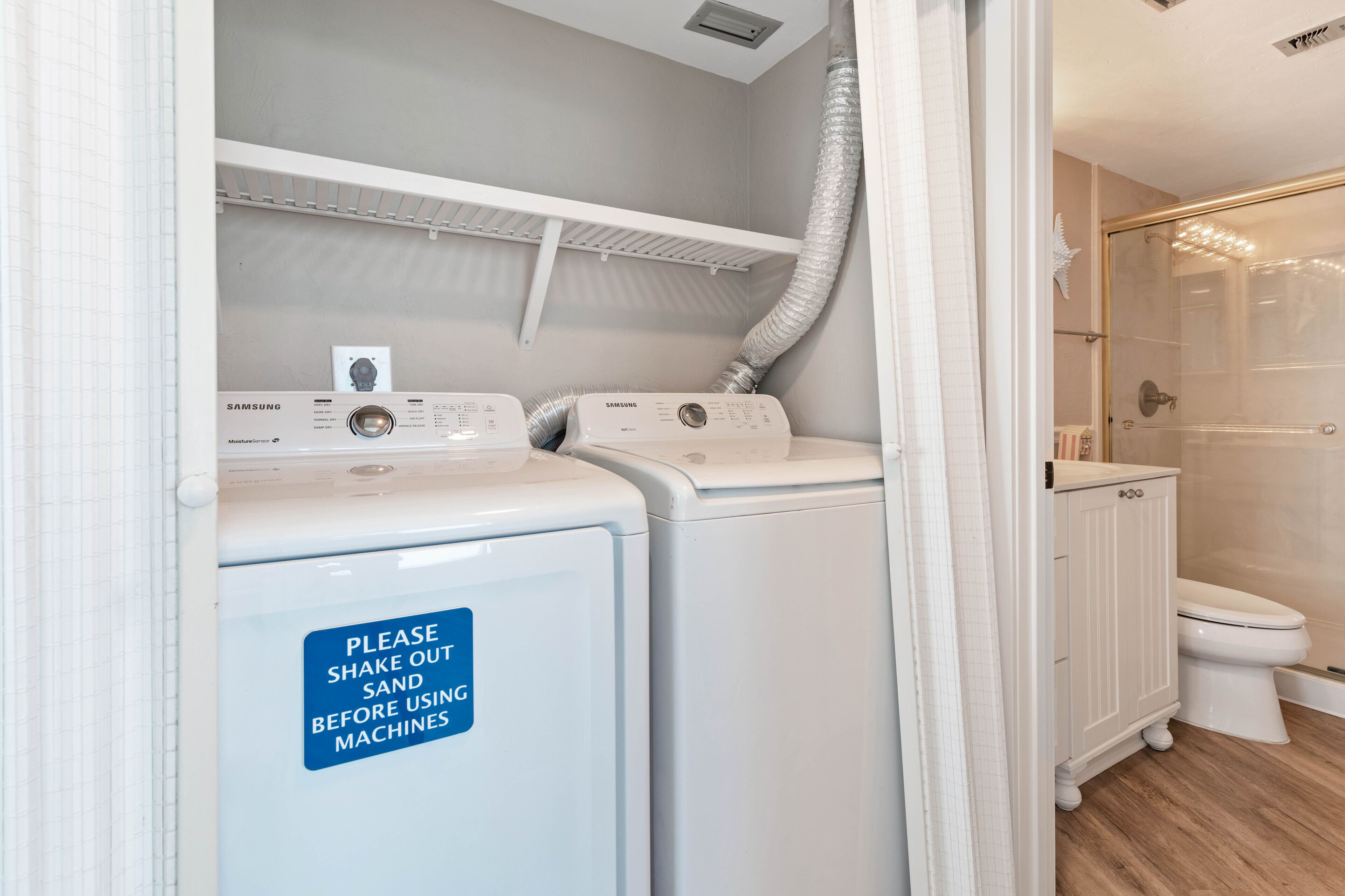 A laundry area with two white washing machines and a sign instructing to shake out clothes before use.