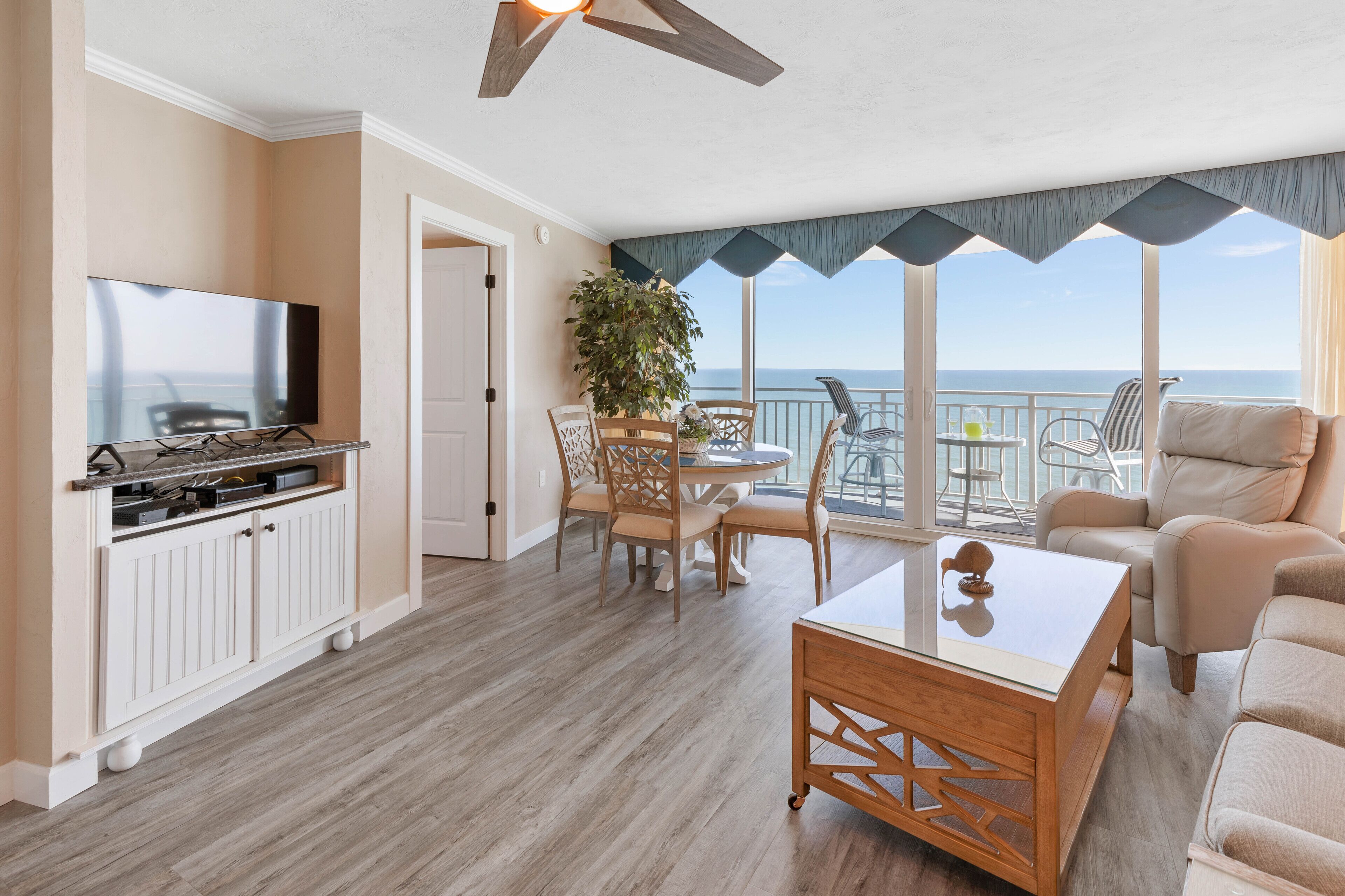 A spacious living area with a balcony, a dining set, and a television.