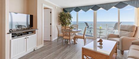 A spacious living area with a balcony, a dining set, and a television.