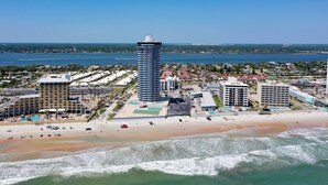 A coastal hotel with a beachfront view, a tall central tower, and a sandy beach.