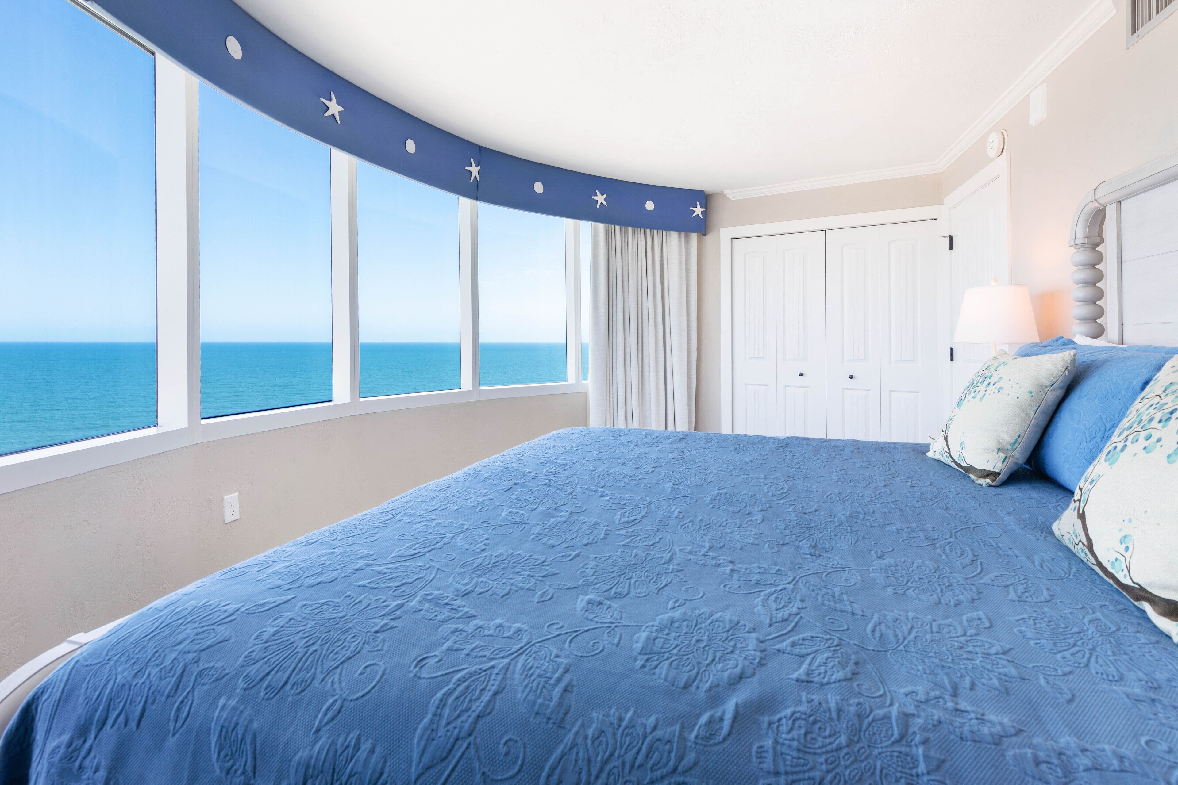 Een slaapkamer met een groot bed, uitzicht op de zee en een gebogen plafond met stersieraden.