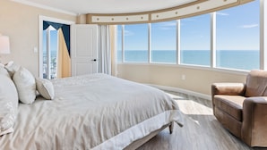A bedroom with a large bed, a chair, and a view of the ocean.