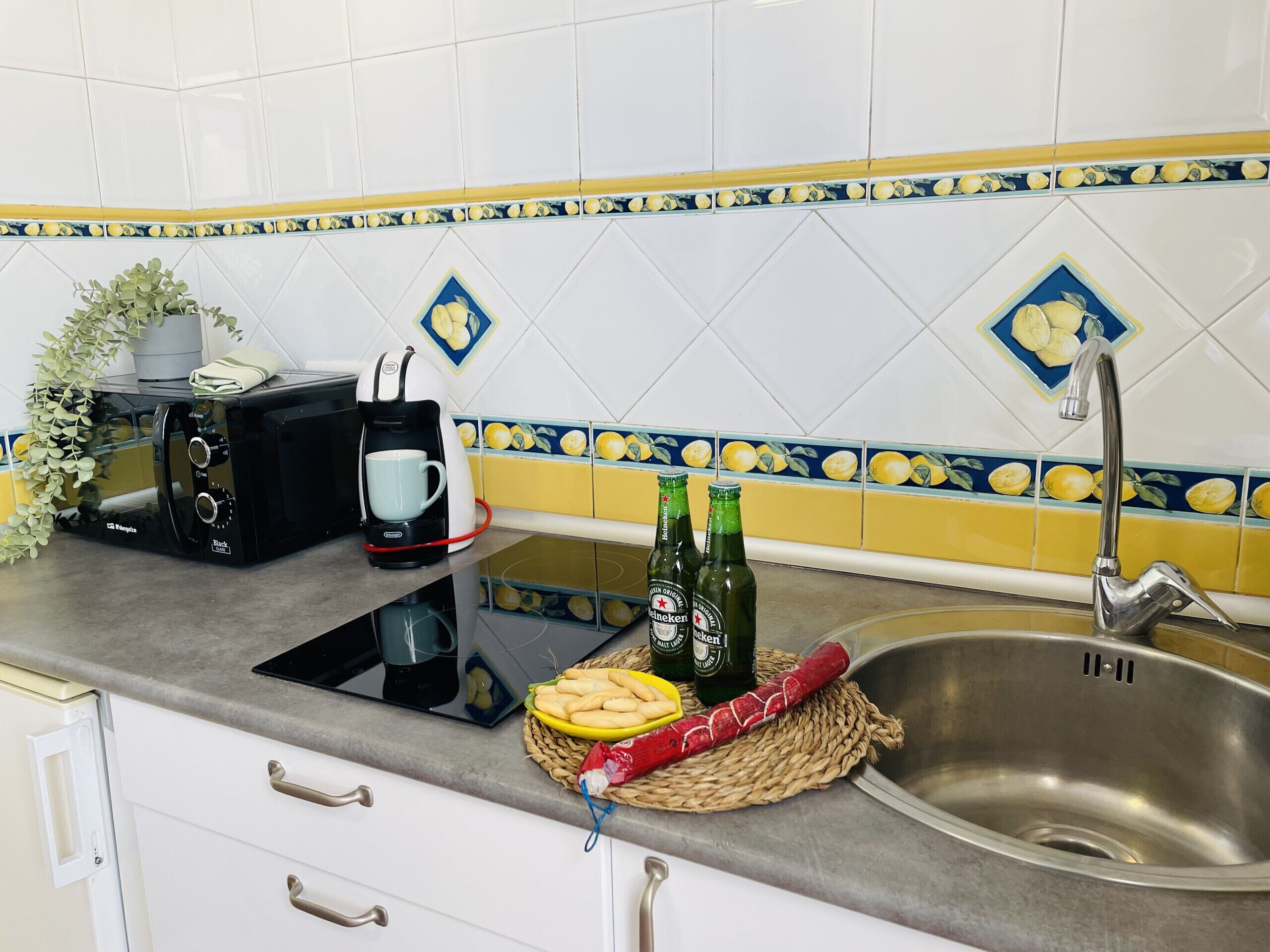 A kitchen with white cabinets, a coffee maker, two beer bottles, a basket of bread, and a red rolling pin on the counter.