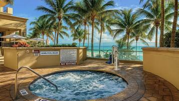 A whirlpool pool with a view of the ocean and palm trees.