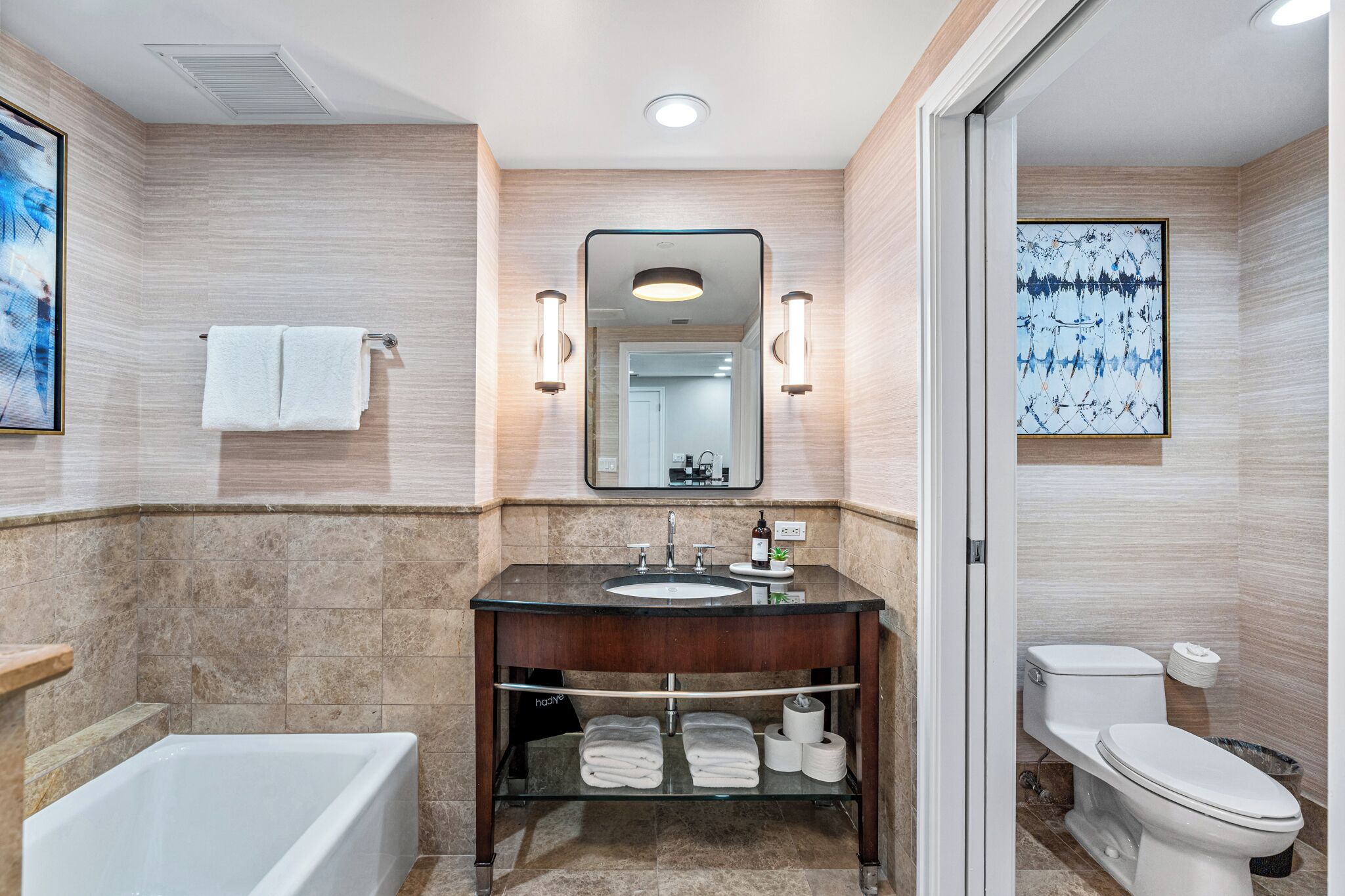 A modern bathroom with a bathtub, a sink with a mirror, and a toilet.