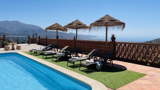 Ein Poolbereich mit Liegestühlen und Sonnenschirmen mit Blick auf eine gebirgige Landschaft.