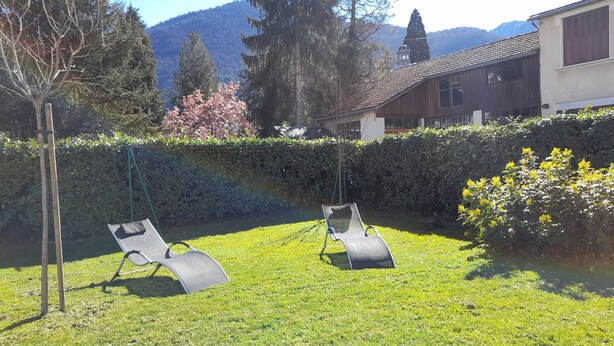 Un giardino sul retro con due poltrone, un prato curato e vista sulle montagne sullo sfondo.
