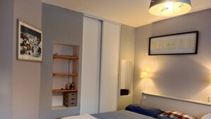 Una camera da letto con un letto, un comodino, una lampada, una mensola con una radio e un quadro appeso al muro.
