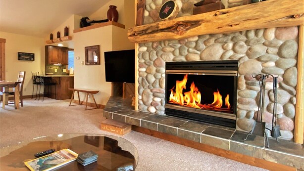 Una sala de estar con chimenea de piedra, televisor y comedor con muebles de madera.