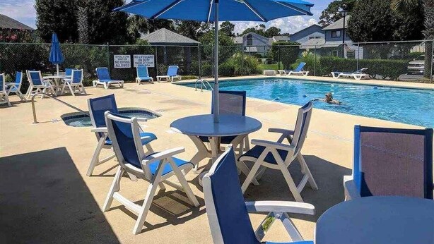 A poolside area with lounge chairs and umbrellas, a pool, and a fence with signs. - 💗☀️🌊Family Fun In The Sun🌊☀️💗 - 3 BR, 3.5 BA & Pet Friendly Townhouse (Little River)