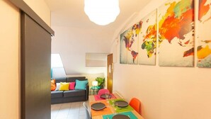 Un comedor con una mesa dispuesta para cuatro personas, cojines de colores en un sofá y arte abstracto en la pared.