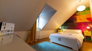 Un dormitorio con techo inclinado, una cama, una mesita de noche, una lámpara y una pared colorida.