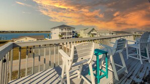 A wooden deck with white and teal chairs, overlooking a coastal area with buildings and a body of water.