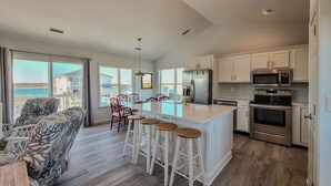 A modern kitchen with a large island, stainless steel appliances, and a view of the sea.