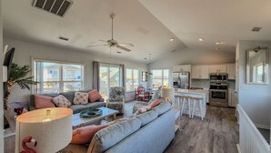 A spacious living area with a sofa, coffee table, and a dining table with chairs. A kitchen with modern appliances is visible in the background.