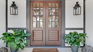 A double wooden door with glass panels, flanked by two lantern-style wall lights, and a welcome mat at the entrance. - Sea la Vie - Luxury Carillon Beach Home - Lake Views! (Panama City Beach)