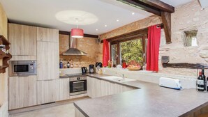 A modern kitchen with wooden cabinets, a built-in oven, a microwave, a large island with a sink, and a stone wall with a window.