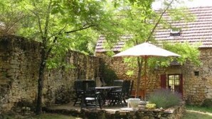A stone building with a tiled roof, a patio with outdoor furniture, and a large umbrella.