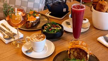 Un tavolo da pranzo con diversi cibi, una teiera e un bicchiere alto con una bevanda rossa.