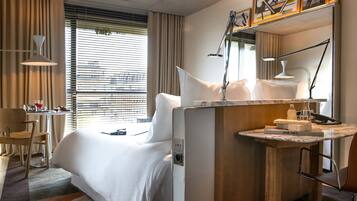 A hotel room with a bed, bedside table, lamp, and a small desk with a chair.