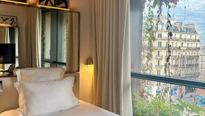 A hotel room with a bed, a large window with curtains, a mirror, and framed artwork on the wall. - Villa M (Paris)