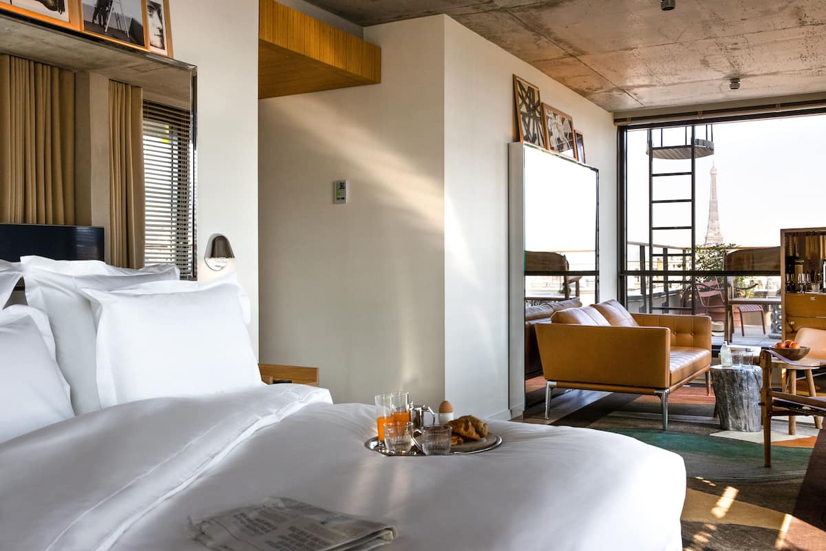 A hotel room with a large bed, a breakfast tray with orange juice, a laptop, and a view of the Eiffel Tower.