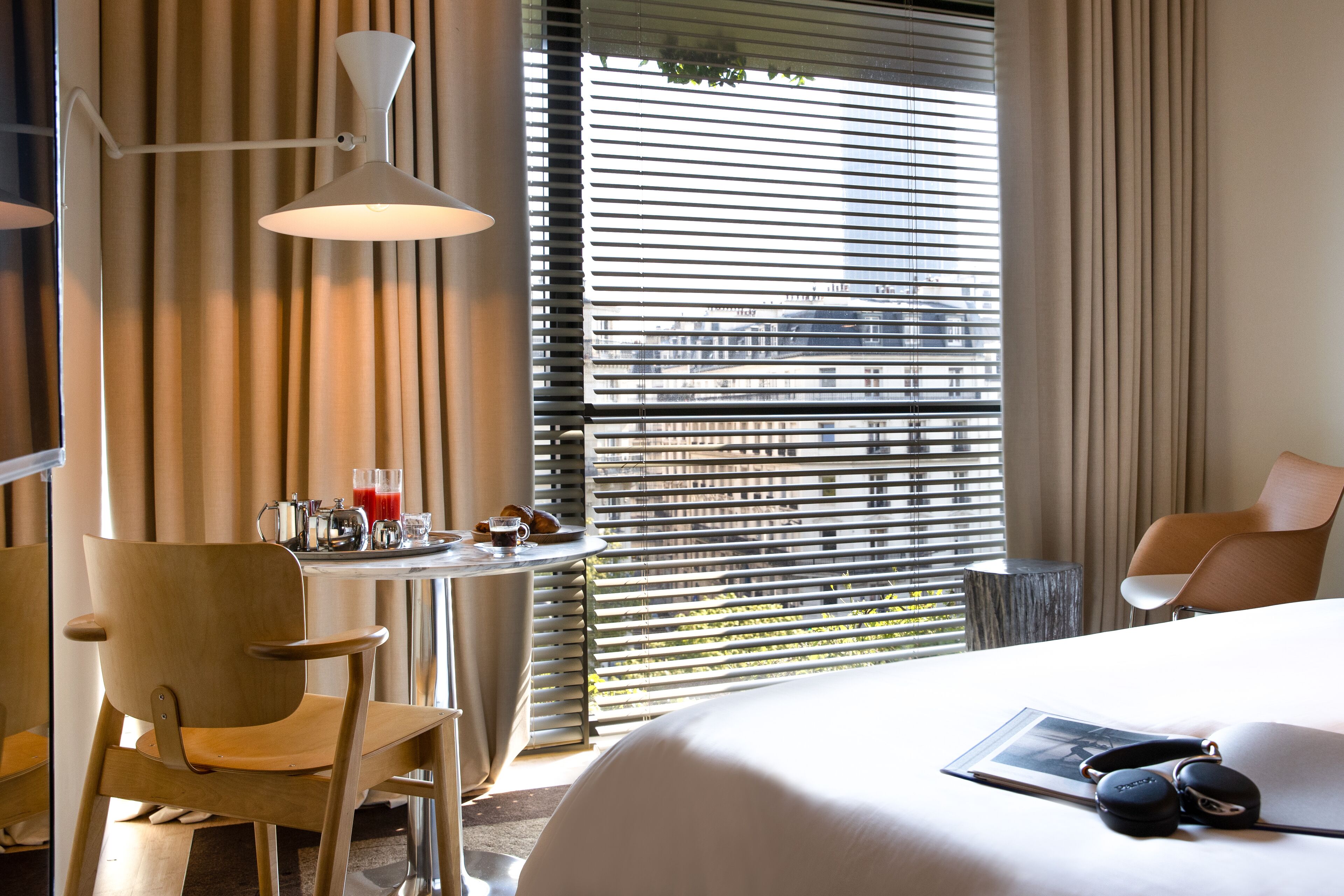 A hotel room with a bed, a chair, a table with a drink, and a window with blinds.