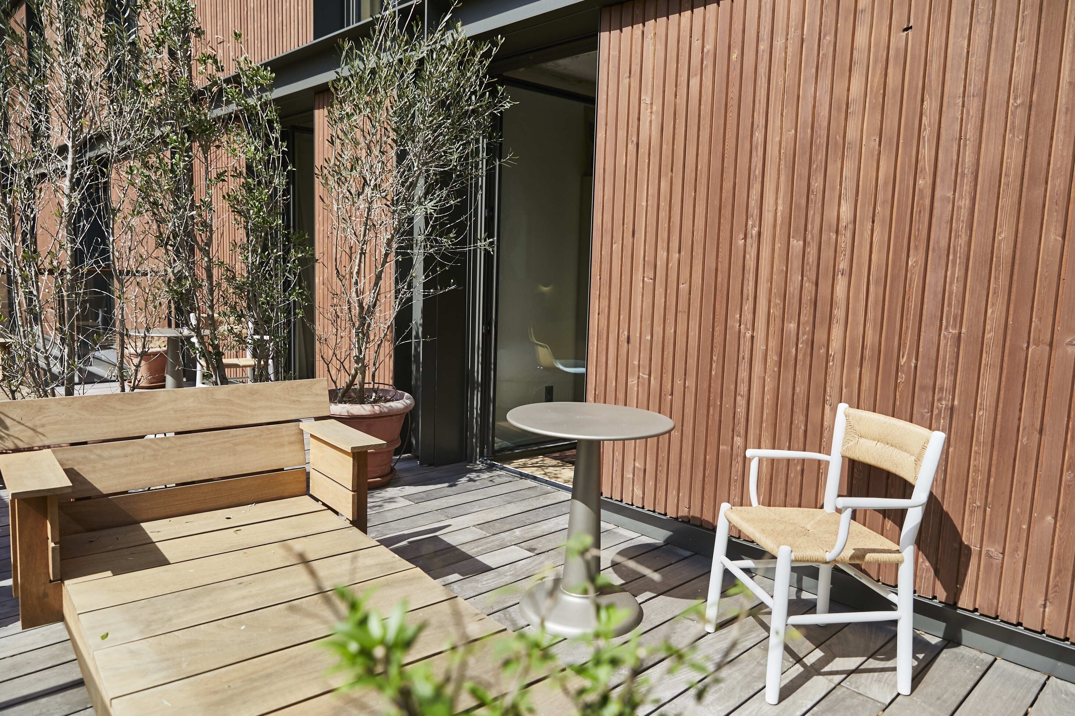 Une terrasse extérieure avec un banc en bois, une chaise blanche et une petite table ronde.
