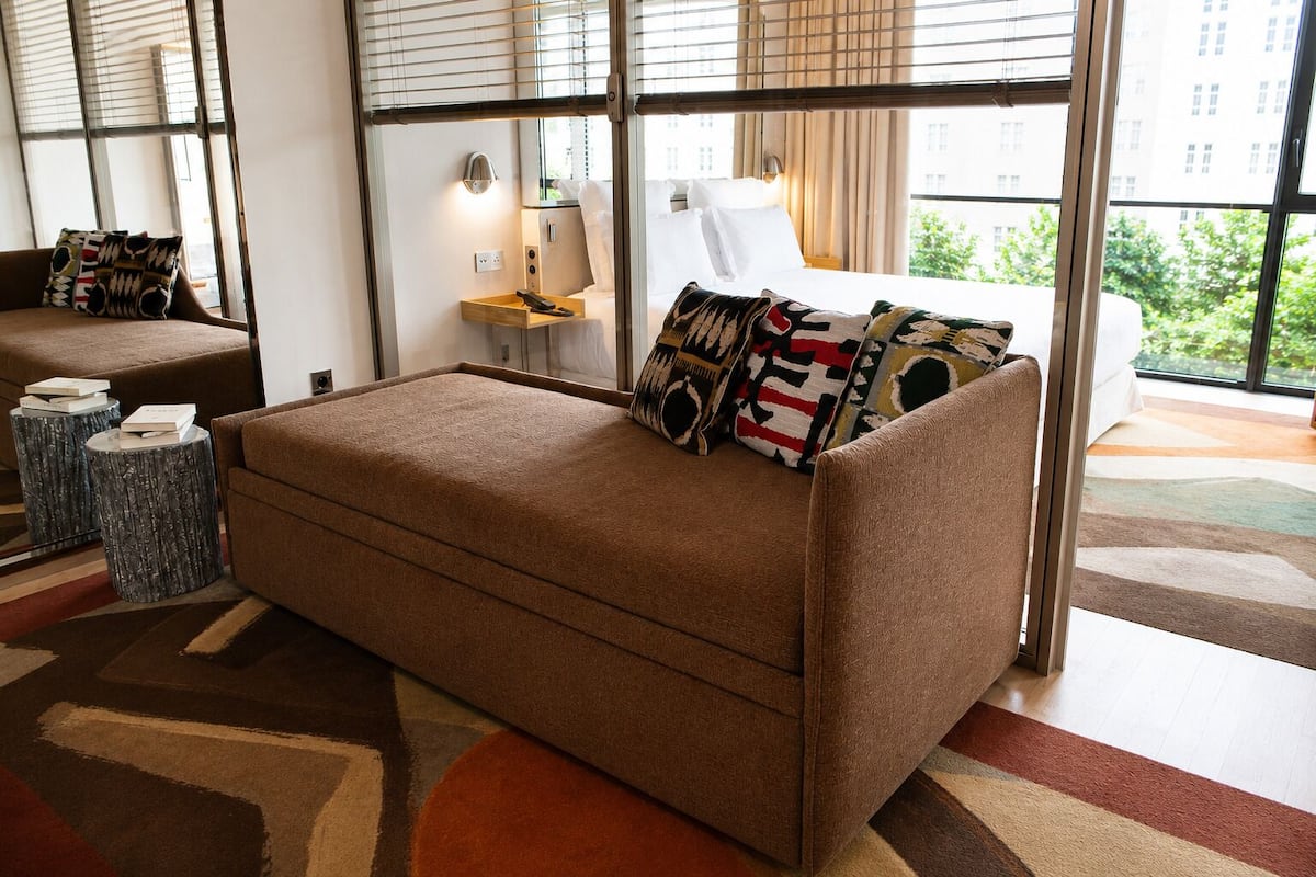 A modern bedroom with a sofa bed, a bedside table with a lamp, and a view through large windows.