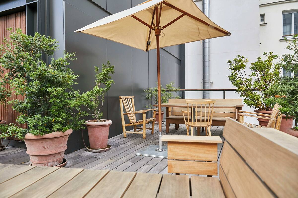 An outdoor patio with wooden furniture, including a table and chairs, and several potted plants.