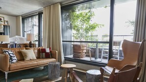 A modern living room with a leather sofa, wooden chairs, a small round table, and a large window with a view of outdoor furniture. - Villa M (Paris)