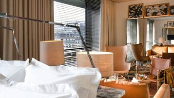 A hotel room with a bed, a desk, a chair, and a large window with blinds.