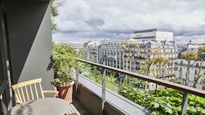 A balcony with a table and chairs, potted plants, and a view of city buildings. - Villa M (Paris)