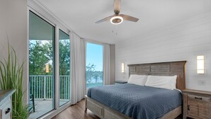 Ein Schlafzimmer mit einem großen Bett, einem Deckenventilator, einem Nachttisch und Blick auf Bäume durch eine Schiebetür.