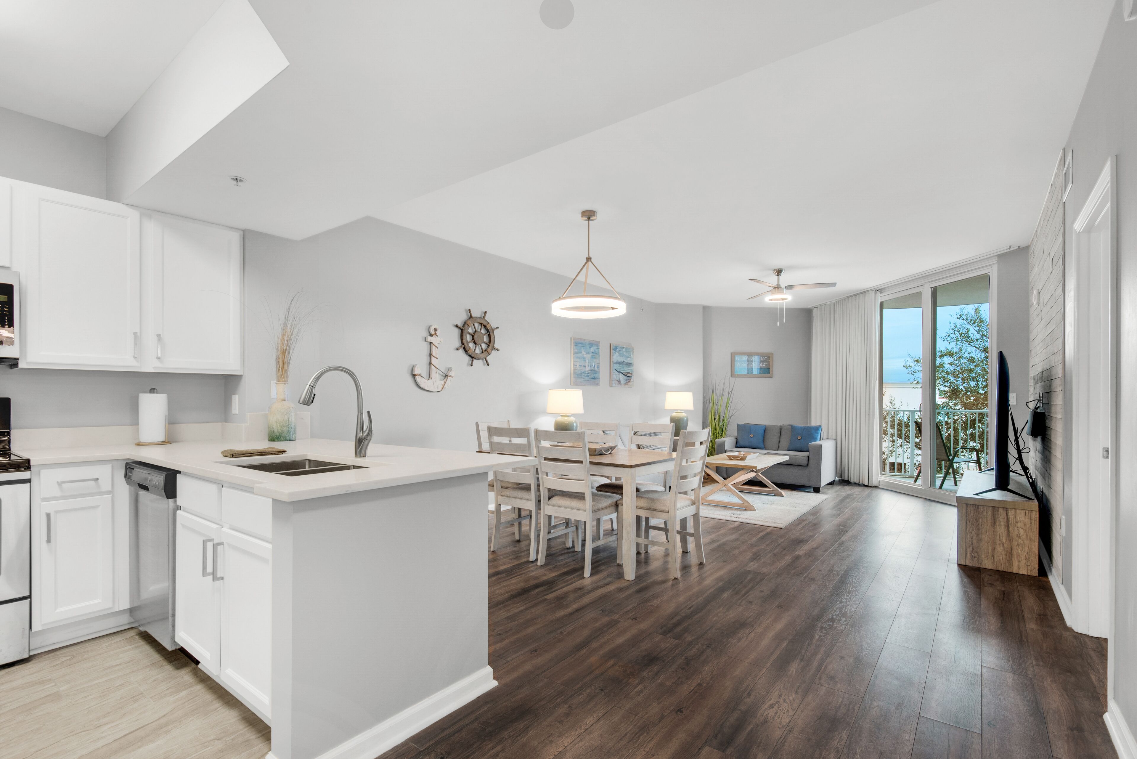 A modern kitchen with white cabinetry, a dining area with a wooden table and chairs, and a large window offering a view of the outdoors.