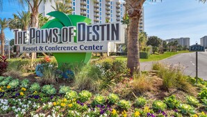 Ein Schild des Palms of Destin Resort & Conference Center mit Blick auf eine Straße und Gebäude im Hintergrund.
