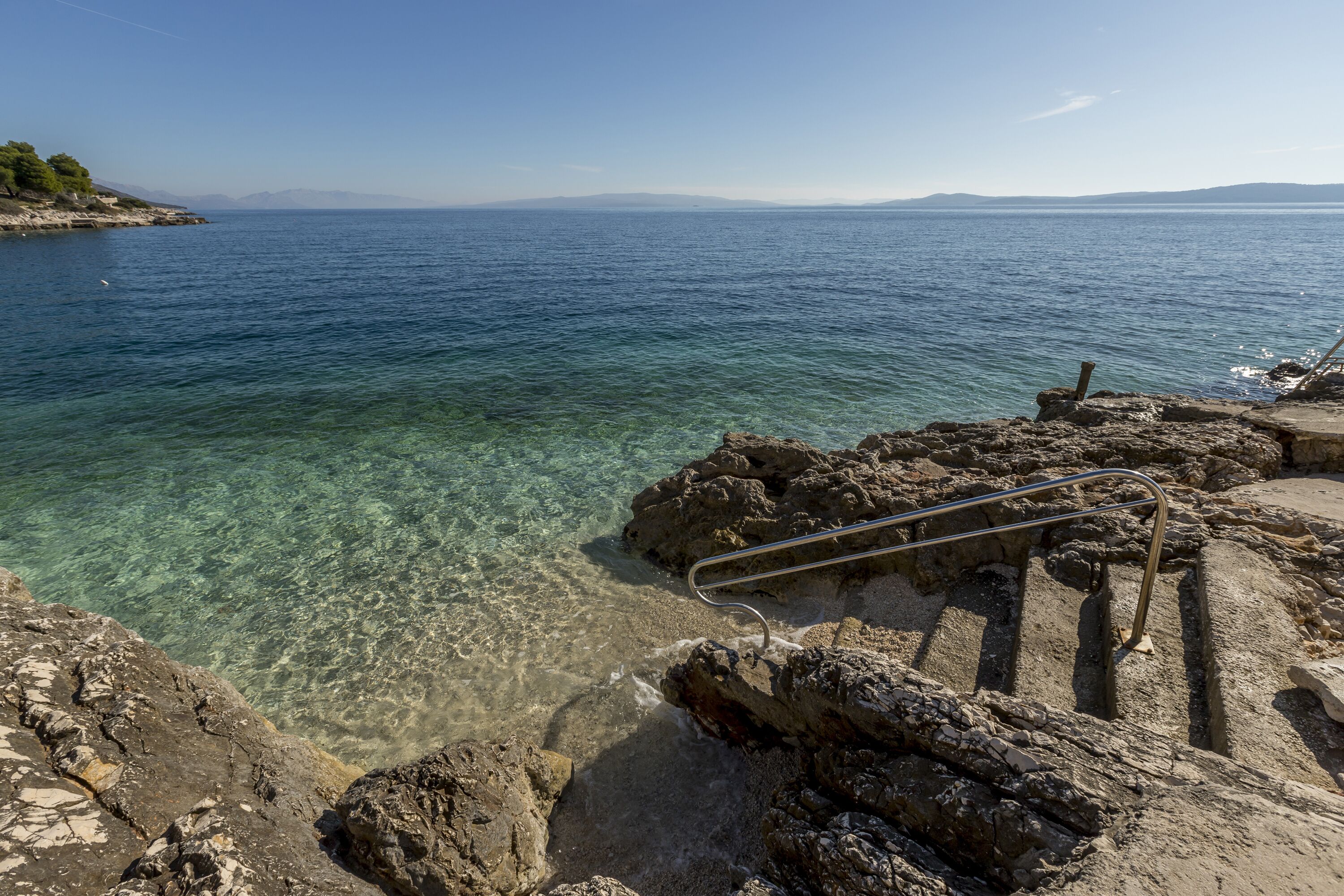 A rocky shoreline with clear water and a metal railing.